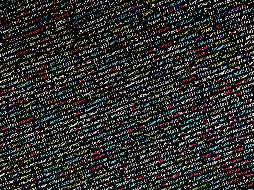 A close-up view of a person's hand wearing a wristwatch, actively typing on a silver laptop keyboard placed on a wooden surface. The laptop screen displays lines of code with syntax highlighted in gre